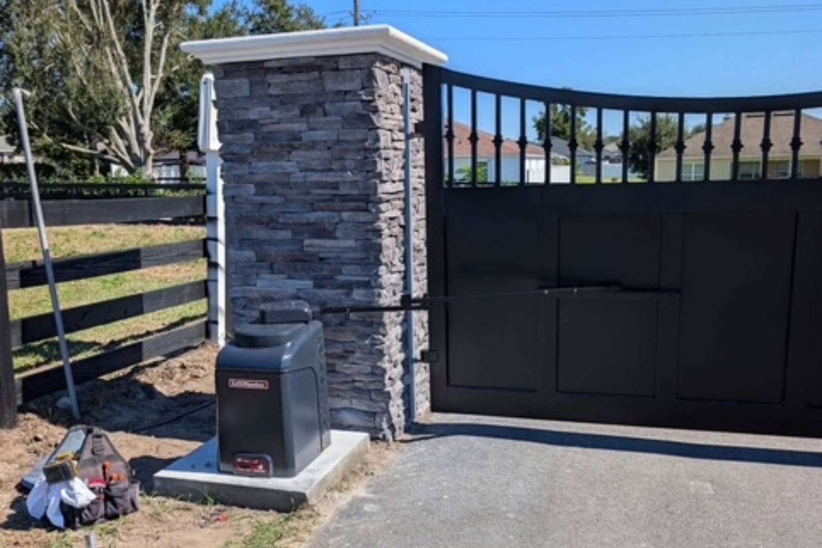 Modern automatic gate opener installed beside a stone pillar and metal gate.