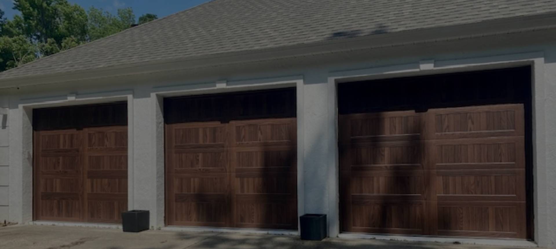 Two closed wooden garage doors under a roof with a small trash bin nearby.