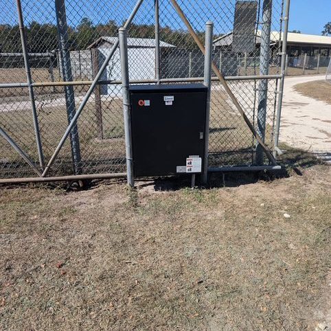 Black metal box mounted on a chain-link fence with a padlock.
